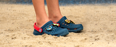 boy's feet standing in the sand with joybees clogs on
