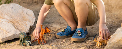 Boy playing in the dirt with dinosaur toys with Joybees skate sneakers and the Dinoland Popinz shoe charms pack